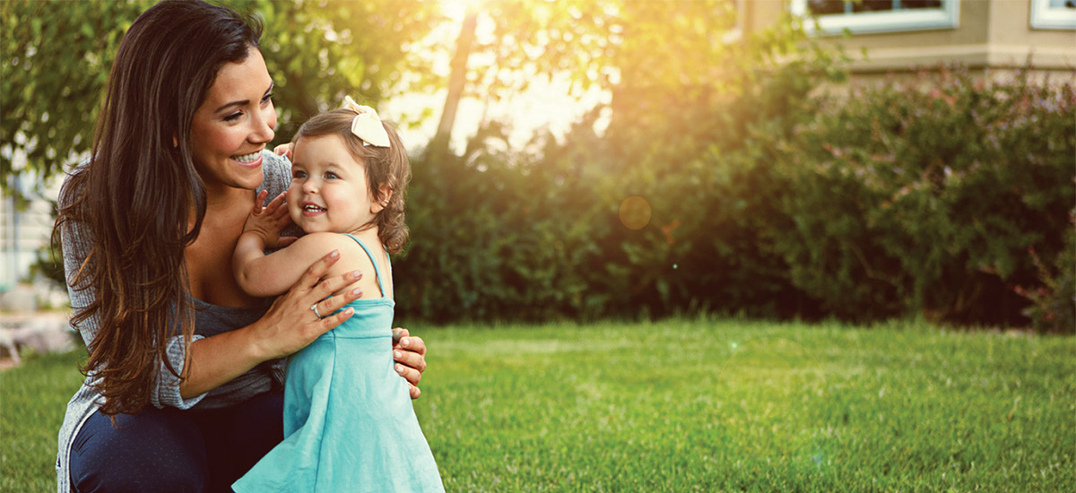 smiling mother holding her young child in the back yard of their home